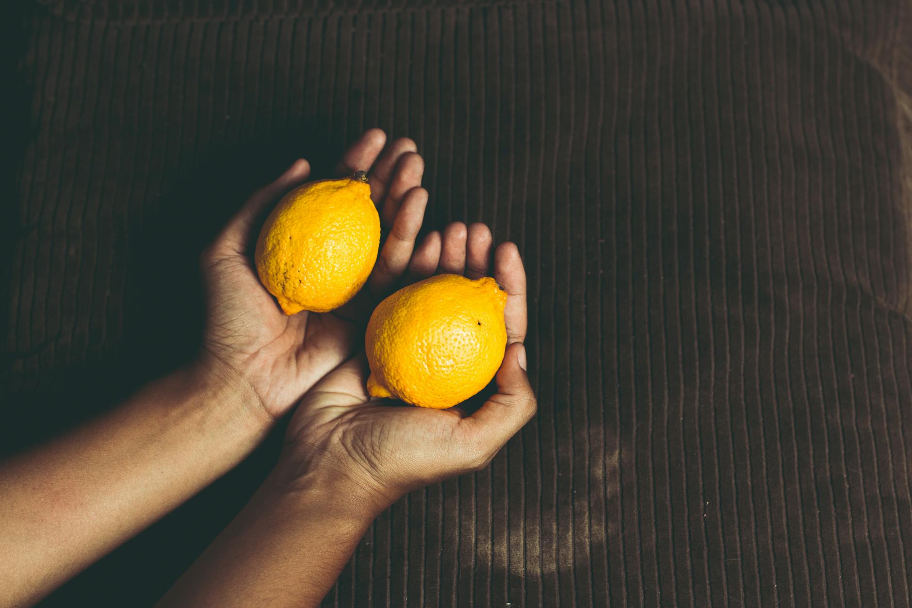 A hand holding a fresh lemon on a soft pink background, symbolizing renewed pleasure and intimacy.