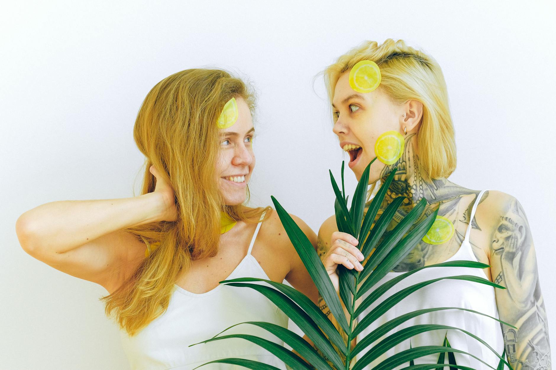 Two women smiling joyfully indoors with tropical plants, expressing authentic pleasure and connection