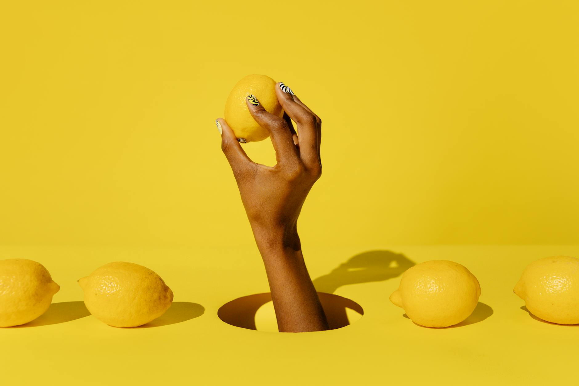 Hand holding a bright lemon against a vivid yellow background, symbolizing fresh pleasure and natural vitality