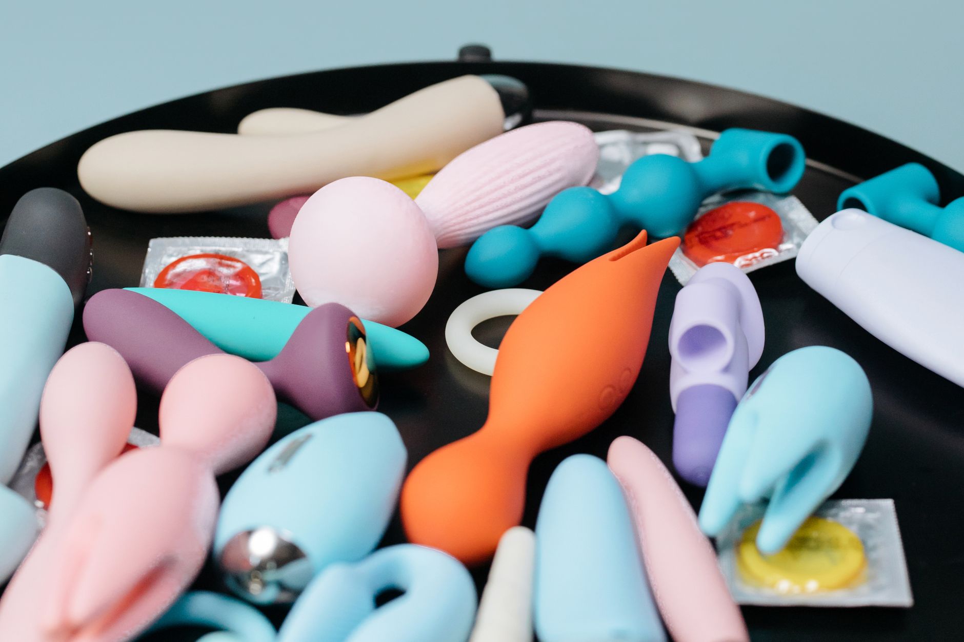 A vibrant collection of various adult toys on a tray, including colorful clitoral vibrators