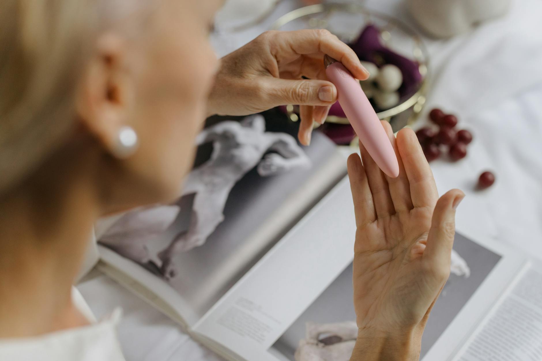 Close-up of a woman holding a personal massager with art books in the background, representing intimate communication and partnership