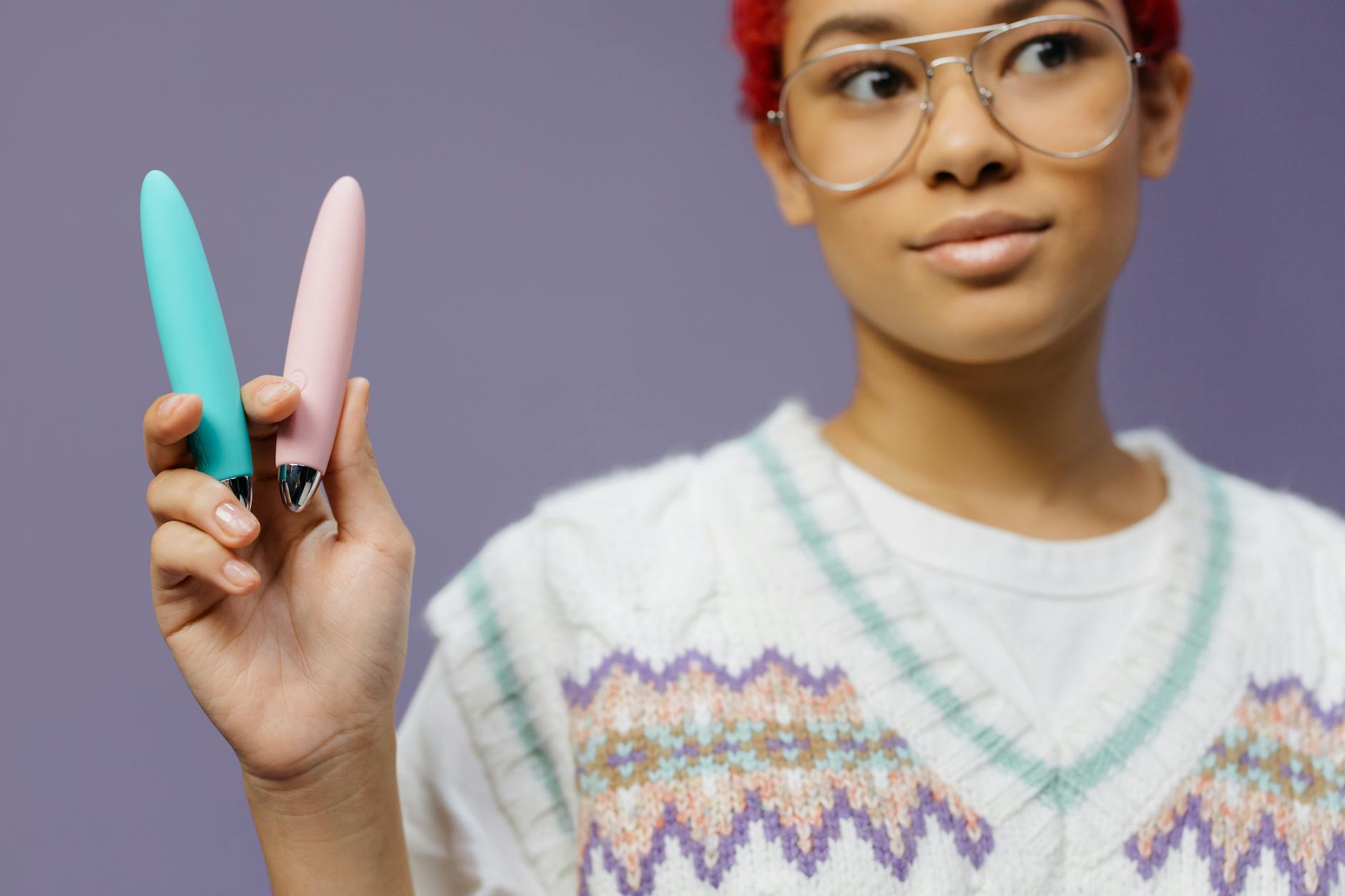A hand holds colorful vibrators against a purple background, symbolizing pleasure recovery options