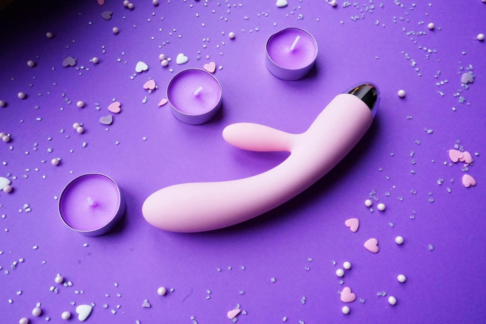 Lemon vibrator on purple background with romantic candles and confetti for sensual intimacy